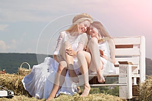 Two girls sitting on bench on hay