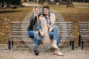 Two girls sitting on the bench outdoors. Autumn weather