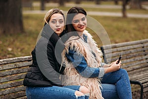 Two girls sitting on the bench outdoors. Autumn weather