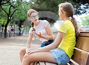 Two girls sitting on bench in park and laughing