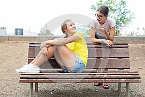 Two girls sitting on bench in park and laughing