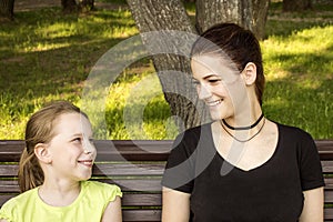 Two girls are sitting on a bench talking and laughing