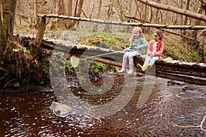 Two Girls Sitting On Bridge Fishing In Stream With Net
