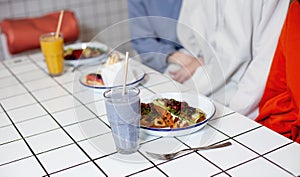 Two girls are sitting in a cafe with food on plates and smoothies on tables in a cafe.