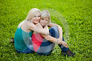 Two girls sitting on the grass, embracing