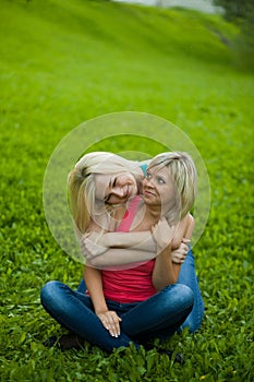 Two girls sitting on the grass, embracing