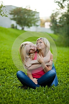 Two girls sitting on the grass, embracing