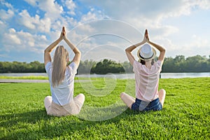 Two girls sitting in lotus position on green grass, back view