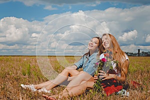 Two girls sitting on meadow with wildflowers and