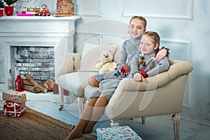 two girls are sitting near the fireplace decorated for Christmas. red-haired sisters smiling, celebrating the new year