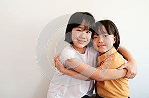 Two girls sitting next to each other hugging each other. showing their connected faces on a white background.