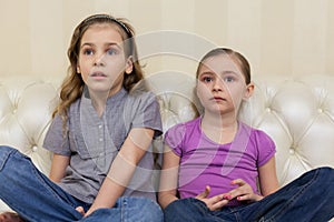 Two girls sitting on a sofa and watching TV intently photo