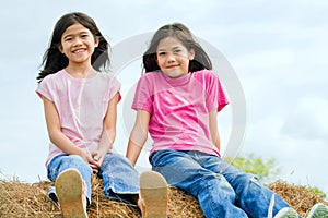 Two girls sitting on top of haybale