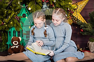 two girls are sitting by the tree. red-haired sisters read a book, celebrating the new year. teddy bear and a castle