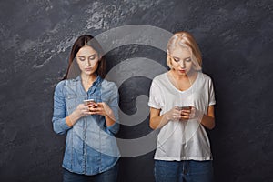 Two girls with smartphones looking in smartphones
