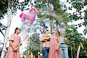 Two girls smashing, hitting pinata with a stick at birthday party. Children celebrating birthday at garden party