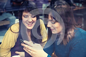 Two girls smiling and using smart phone in a cafe