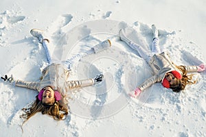 Two Girls on a snow angel shows. Children playing and making a snow angel in the snow. Top view.