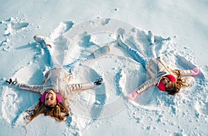 Two Girls on a snow angel shows. Children playing and making a snow angel in the snow. Top view.