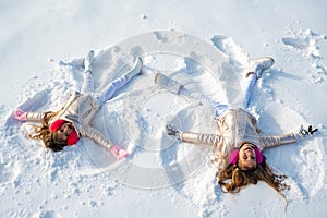 Two Girls on a snow angel shows. Children playing and making a snow angel in the snow. Top view.