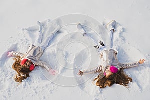 Two Girls on a snow angel shows. Smiling children lying on snow with copy space. Children playing and making a snow