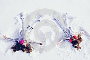 Two Girls on a snow angel shows. Smiling children lying on snow with copy space. Children playing and making a snow