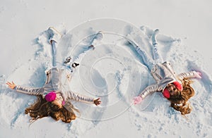 Two Girls on a snow angel shows. Smiling children lying on snow with copy space. Children playing and making a snow