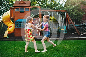 Two girls splashing each other with gardening house on backyard on summer day