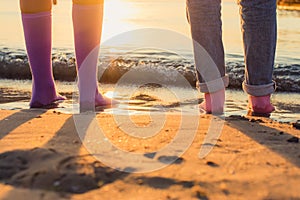 two girls stand on the beach in socks on their bare feet. close-up at sunrise.