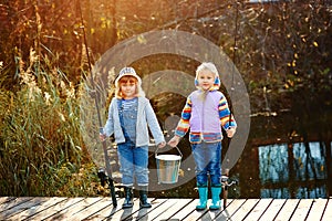 Two girls stand on the bridge and hold in their hands fishing rods and a bucket for fish