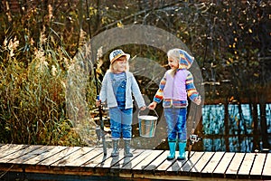 Two girls stand on the bridge and hold in their hands fishing rods and a bucket for fish