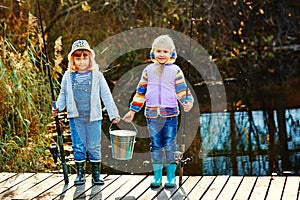 Two girls stand on the bridge and hold in their hands fishing rods and a bucket for fish