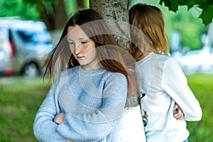 Two girls in summer in the park. The concept of school friends in a quarrel, a problem teenager. Emotions of conflict