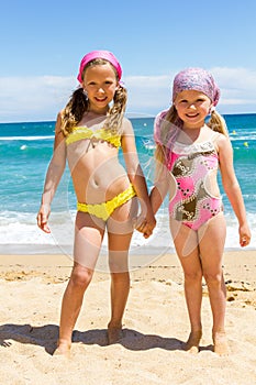 Two girls in swimwear on beach.