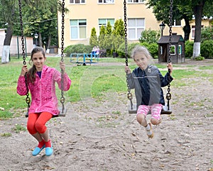 Two girls swing on a swing. Playground