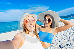 Two girls taking a self-portrait with cell wearing blue casual summer clothes and funny sunglasses on vacation at tropical beach