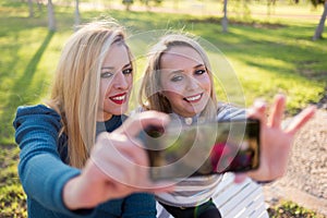 Two girls taking a selfie in the park. Smiling for smartphone photography