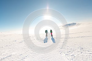 two girls are talking while hiking in the winter mountains. Two young girls in snowshoes and with backpacks stand on a pass in the