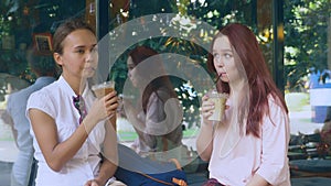 Two girls are talking in an outdoor cafe. they drink cocktails on the street. 4k, slow-motion shooting.