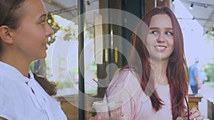 Two girls are talking in an outdoor cafe. they drink cocktails on the street. 4k, slow-motion shooting.