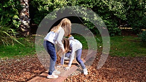 Two girls teetering on an unstable log, playing in the park. active games.