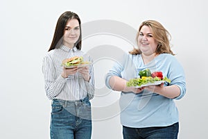 Two girls, thick and thin, with healthy food from vegetables and fruits and unhealthy fast food with a hamburger. The