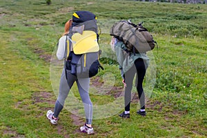 Two girls tourists with backpacks go on the road covered with st