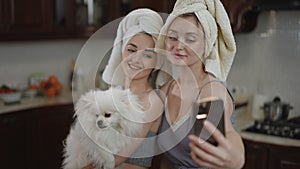 Two girls with towels on their heads and a dog in their arms take a selfie on a mobile phone camera while standing in a