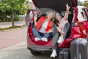 Two girls in trunk of red car posing for camera