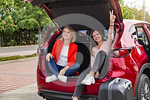 Two girls in trunk of red car posing for camera