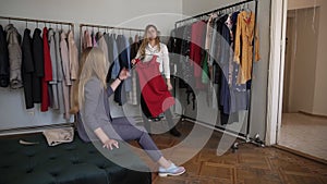 Two girls or twin sisters shopping together: attractive young blonde female is trying a new red dress while standing