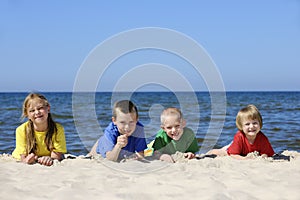 Two girls and two boys in colorful t-shirts lying on sandy beach