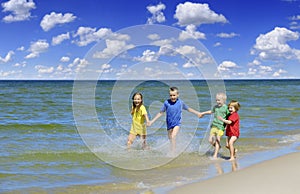 Two girls and two boys in colorful t-shirts running on a sandy beach