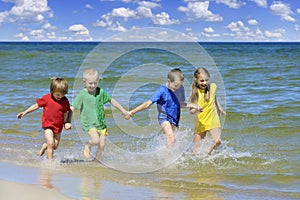 Two girls and two boys in colorful t-shirts running on a sandy beach